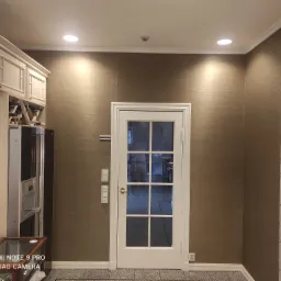 Wnętrze kuchni z widoczną tapetą w odcieniach brązu, białe meble kuchenne i przeszklone drzwi wewnętrzne.