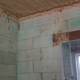 MIK-MONTAŻ Sp.z.o.o. - Wewnętrzne ściany z betonu komórkowego w trakcie budowy, widoczne białe rurki instalacji poprowadzone po ścianach i pod sufitem, sufit ocieplony pianą PUR.