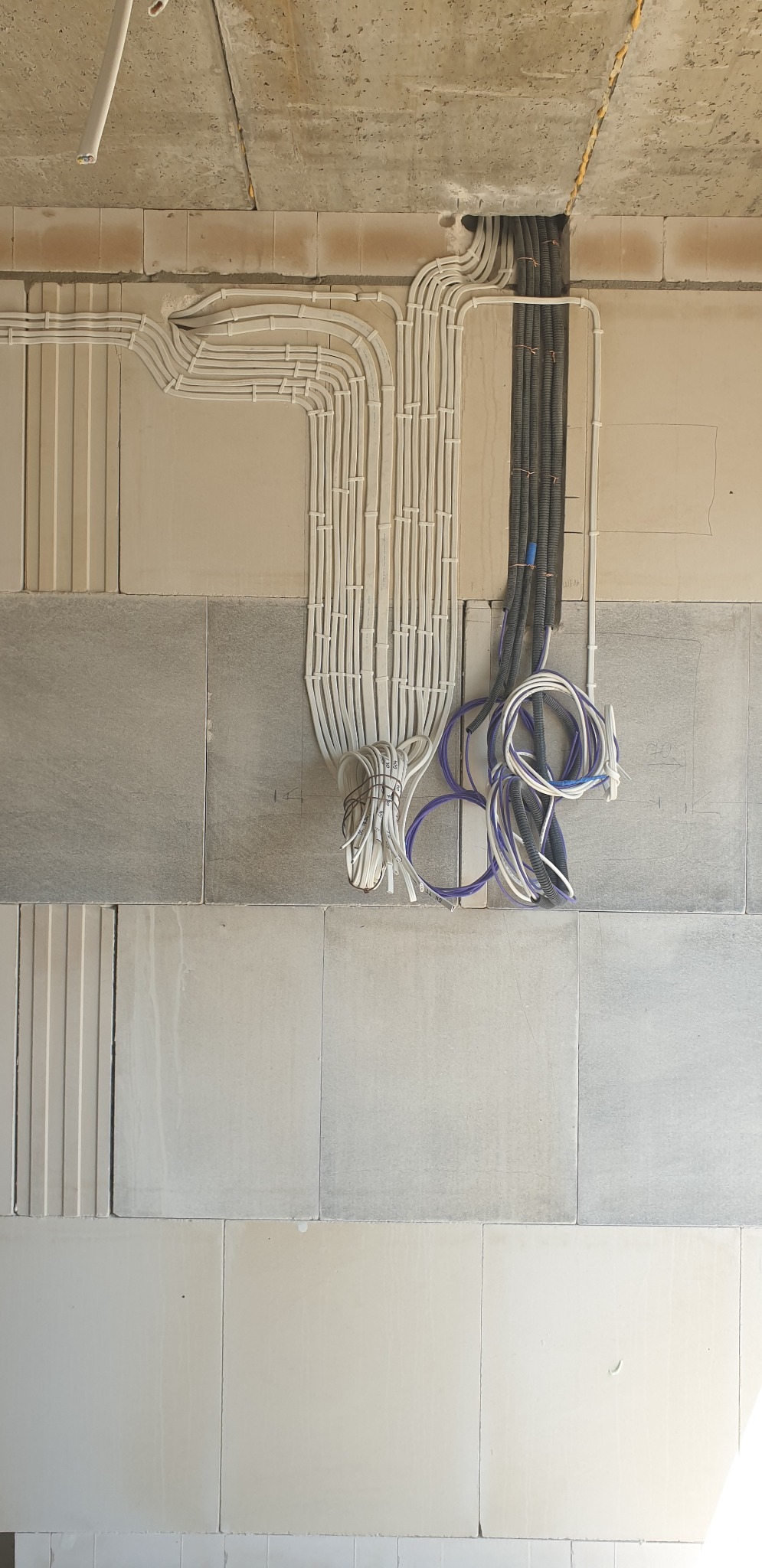 Kable elektryczne prowadzone w peszlach i rurkach, część ułożona wzdłuż ściany i sufitu, część zwisająca w pętlach, widoczne oznaczenia na ścianie.