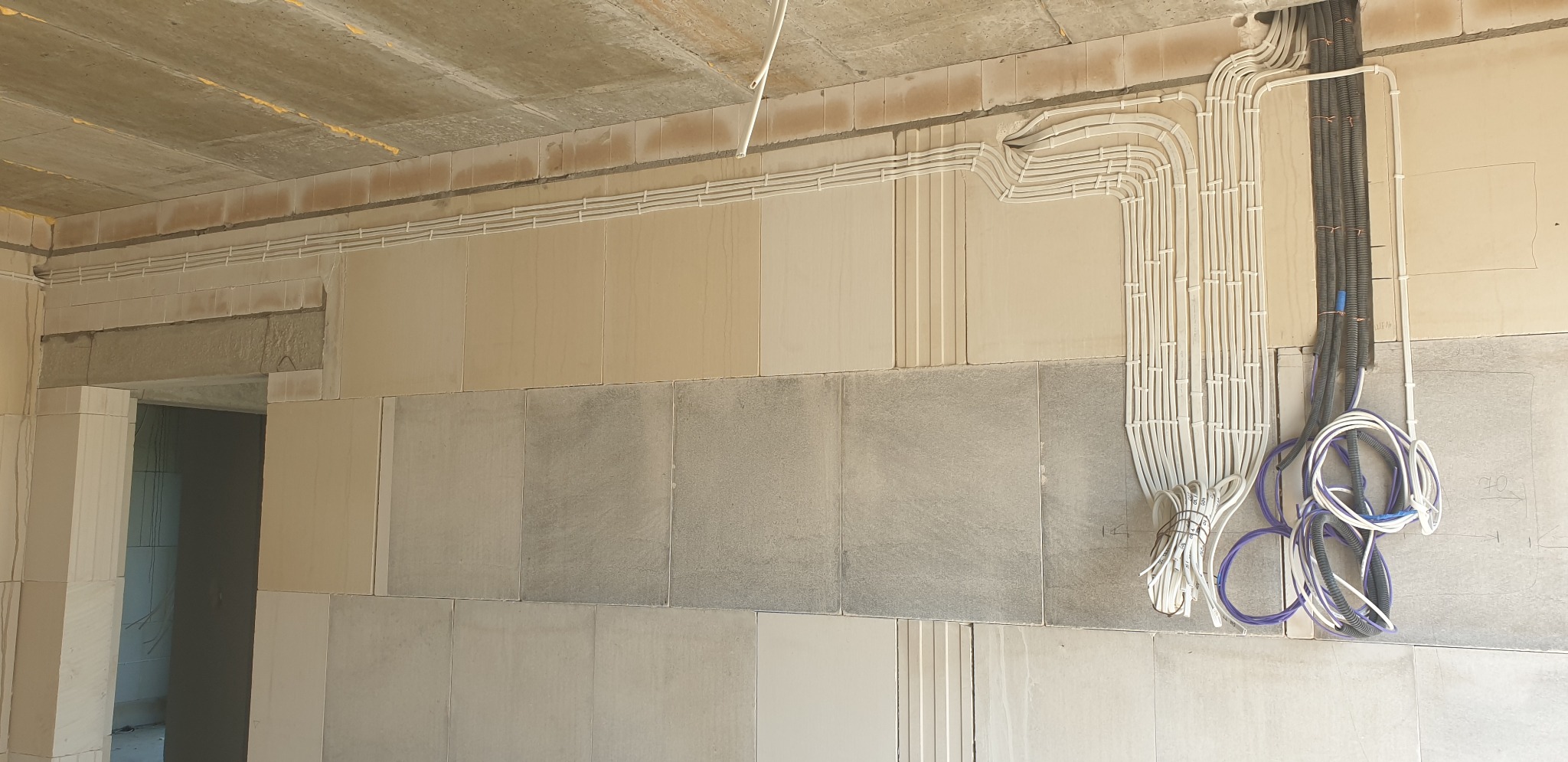 Wewnętrzne kable i przewody prowadzone wzdłuż surowych ścian z betonu komórkowego, z widocznymi wiązkami przewodów zasilających i telekomunikacyjnych.