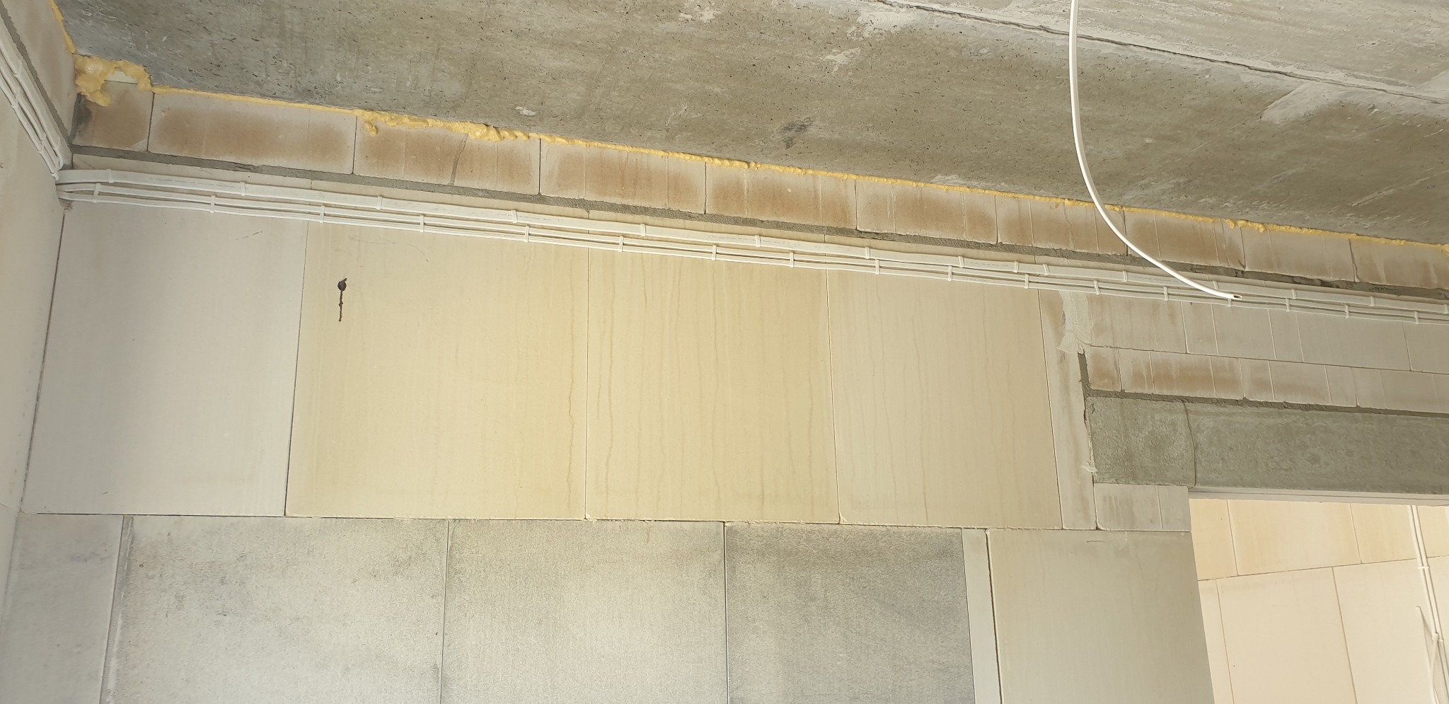 Wewnętrzne kable w białych listwach na ścianie z pustaków, widoczne pianka montażowa i surowy betonowy strop.