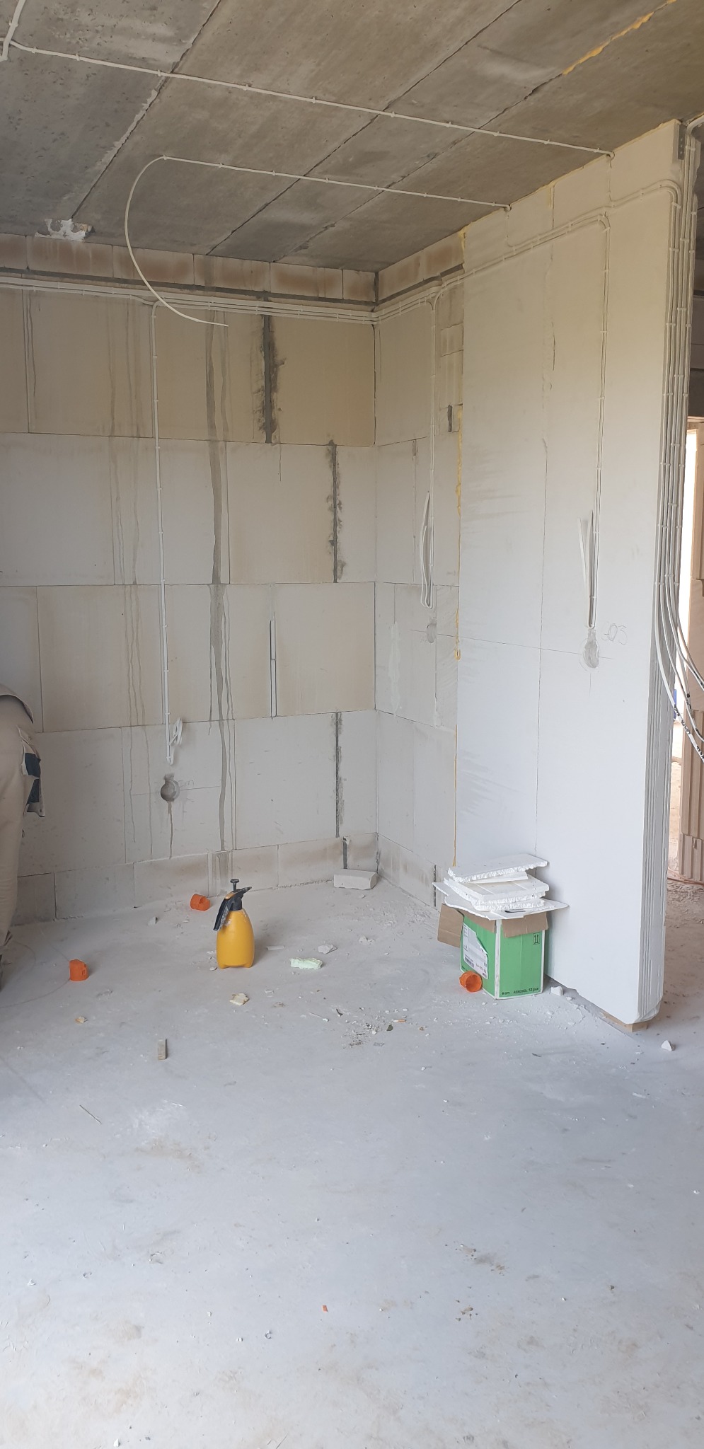 Wnętrze surowego budynku w trakcie instalacji elektrycznej; widoczne przewody elektryczne prowadzone pod sufitem i wzdłuż ścian z betonu komórkowego, żółty opryskiwacz ciśnieniowy i kartonowe...