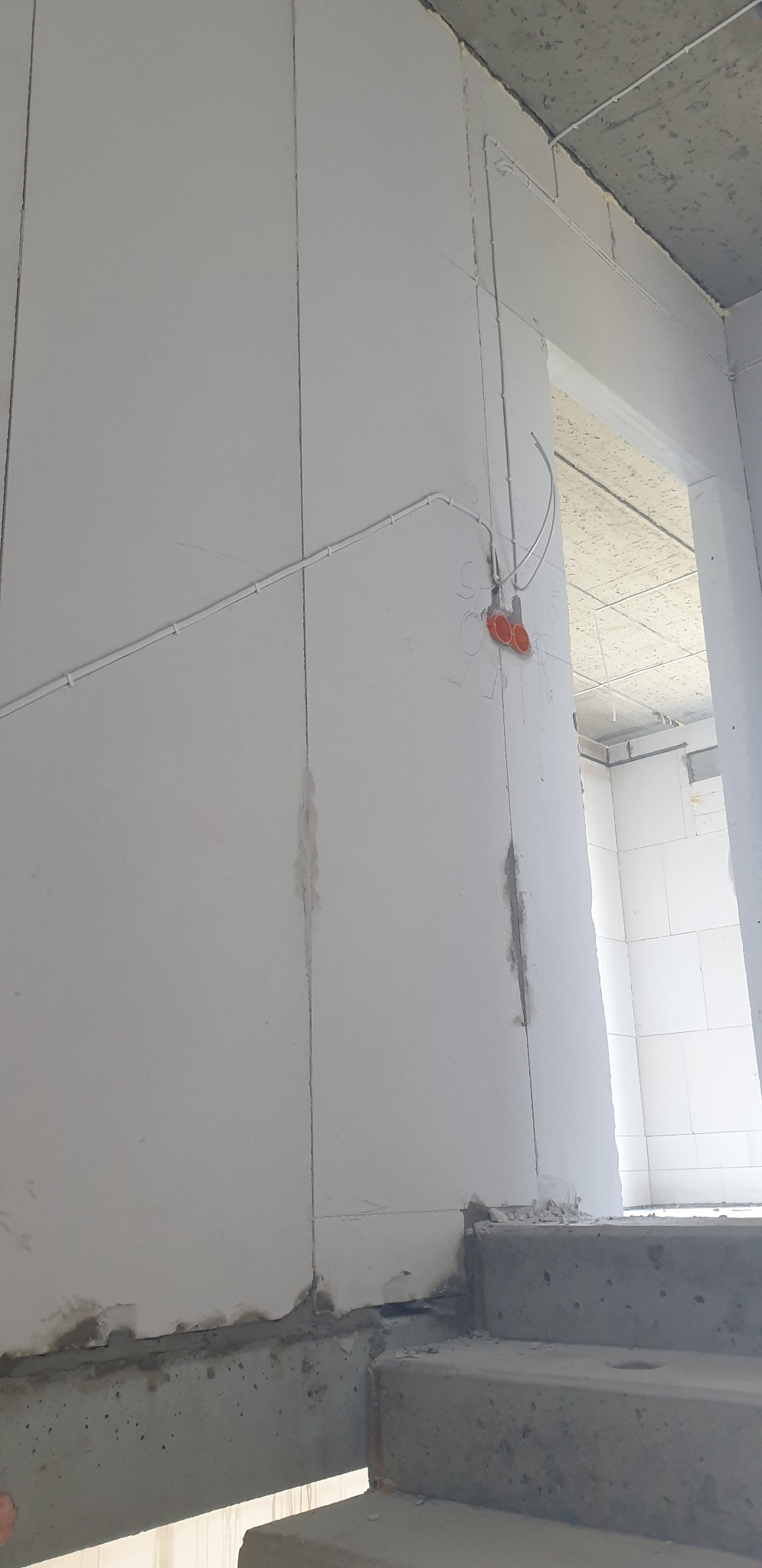 Surowy stan instalacji elektrycznej w nowym budynku w Warszawie: widoczne przewody prowadzone po ścianie, puszki podwójne w kolorze pomarańczowym, ściany z betonu komórkowego, sufit betonowy.