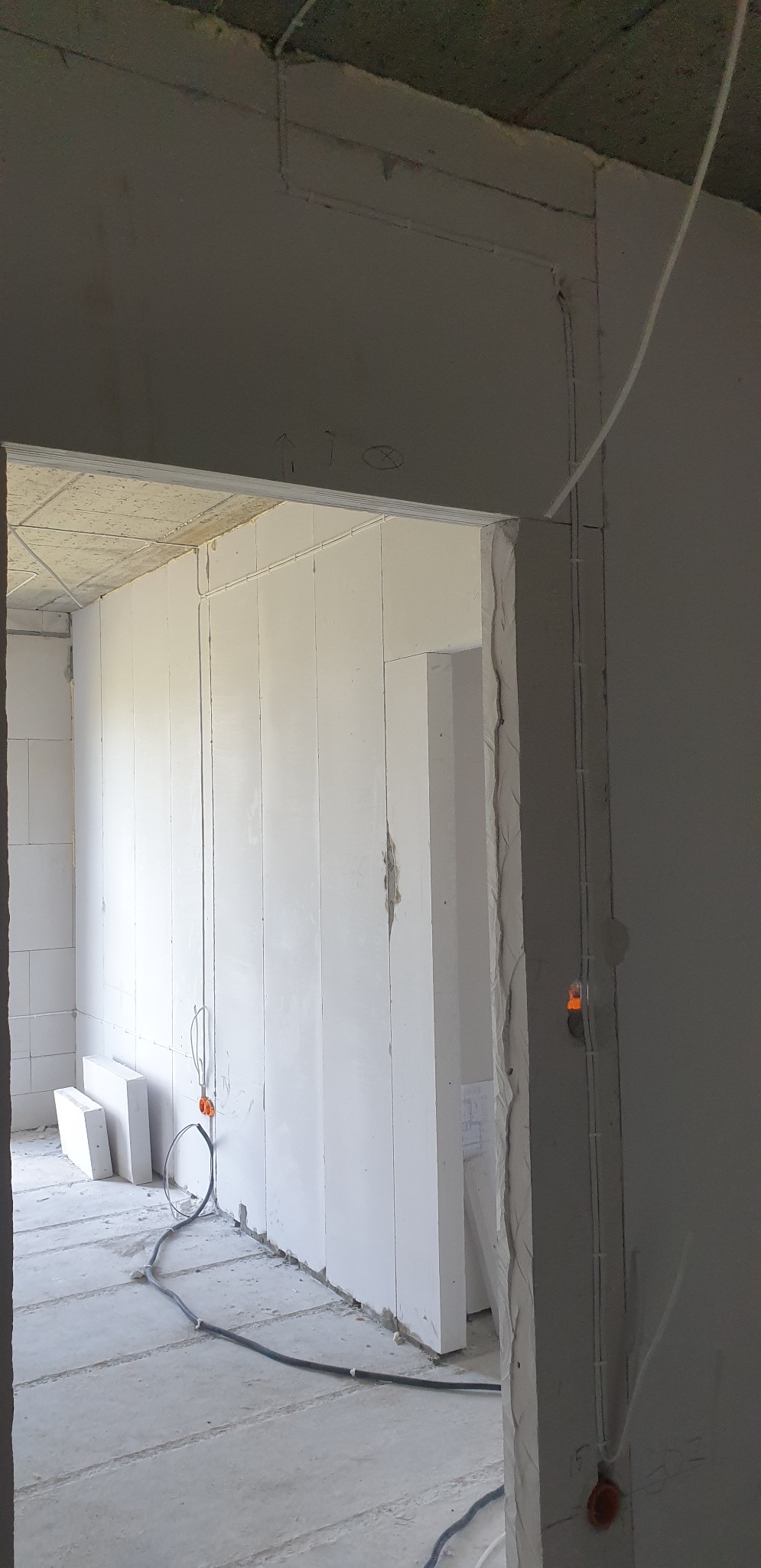 Wnętrze w trakcie prac wykończeniowych, widoczne kable elektryczne prowadzone po ścianie w peszlu, ściany z białych bloczków, surowy betonowy sufit i podłoga.