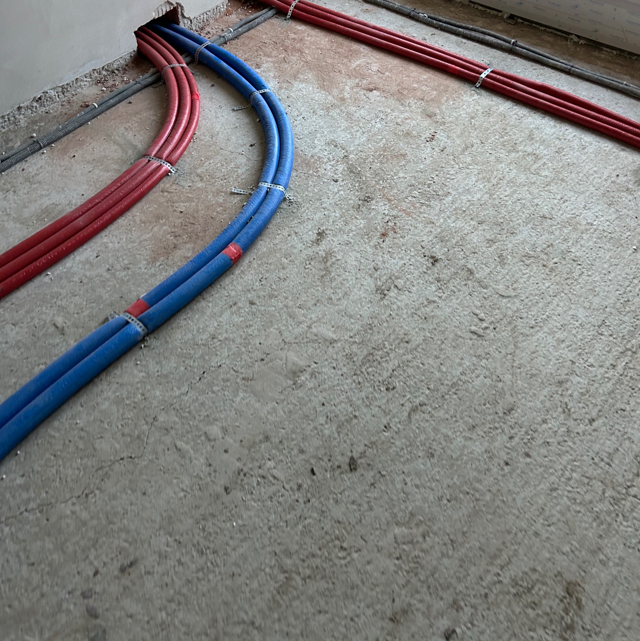Instalacja ogrzewania podłogowego w Krosno: czerwone i niebieskie rury zamocowane do podłoża, gotowe do zalania. Widok z góry na surowy beton.