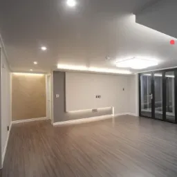 Nowoczesne wnętrze po remoncie z drewnianą podłogą, oświetleniem LED pod ścianą, i ścianą z wzorem jodełki w oddzielnym pomieszczeniu.