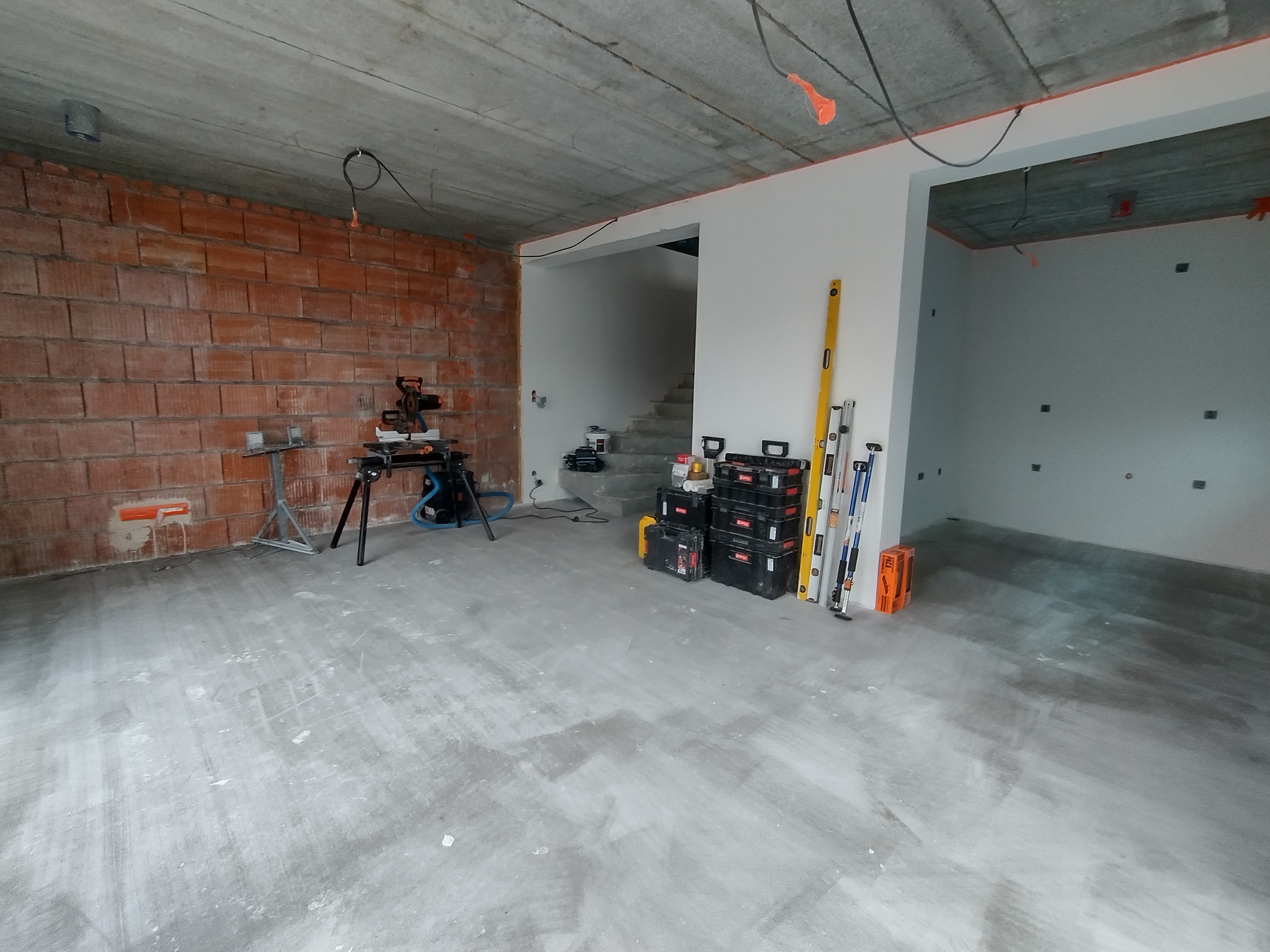 Wnętrze w stanie surowym z widoczną ścianą z czerwonej cegły, betonowym sufitem, narzędziami i skrzynkami narzędziowymi przygotowanymi do prac wykończeniowych.