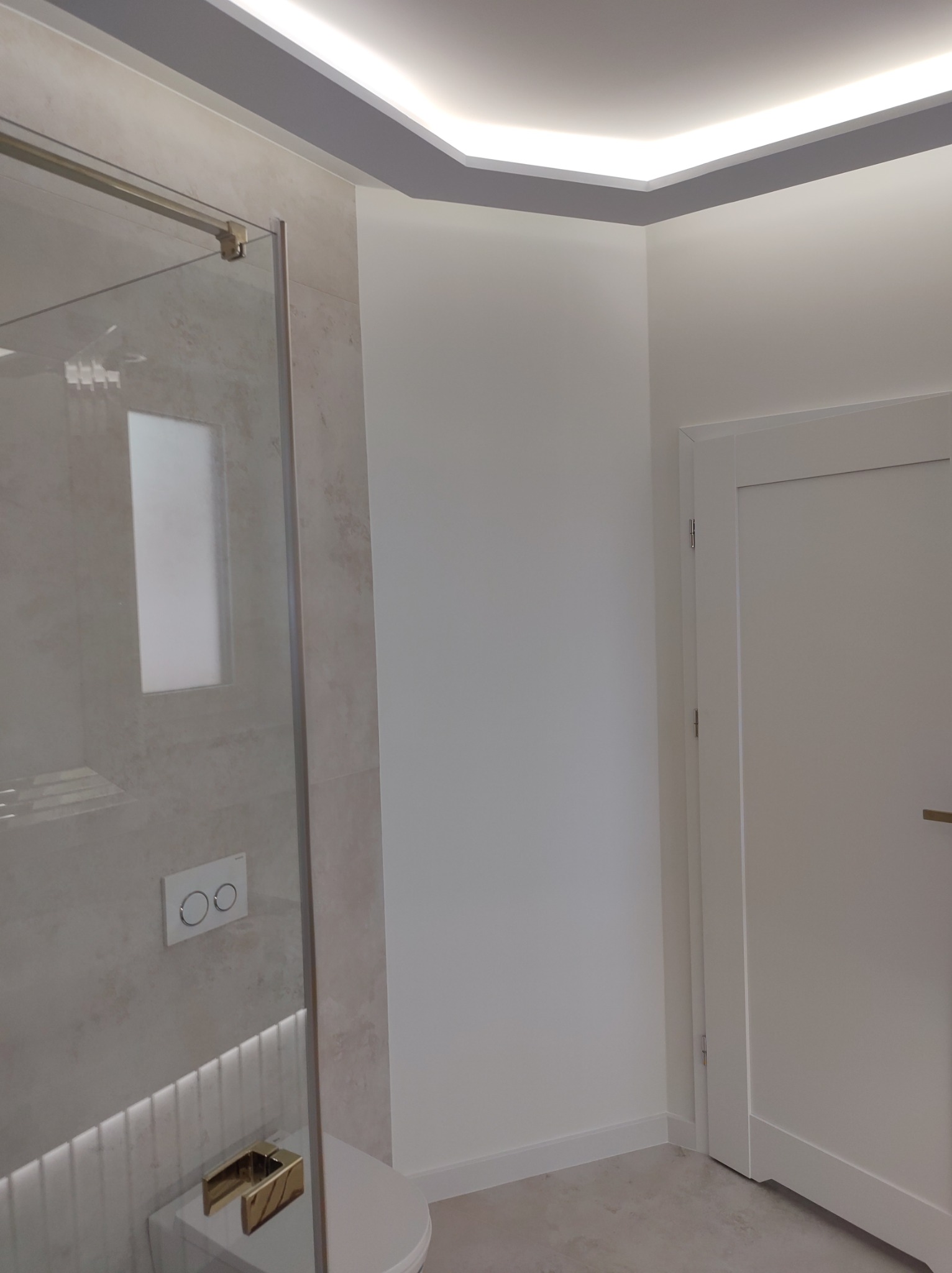 Nowoczesna łazienka z kabiną prysznicową ze szklanymi drzwiami, podświetlanym sufitem i białymi ścianami oraz ukrytą spłuczką WC.