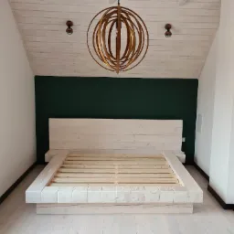 Rama łóżka z bielonego drewna z prostym zagłówkiem na tle ciemnozielonej ściany, z drewnianym żyrandolem i lampami sufitowymi, widok z przodu.