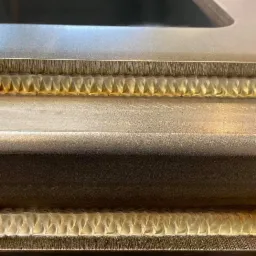 Precyzyjny spaw na metalowej konstrukcji z widocznym rowkiem, ukazujący regularne spoiny o złotym odcieniu.