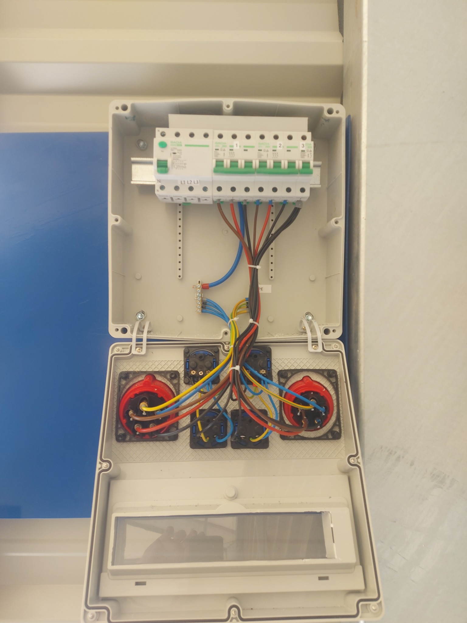 Otwarta skrzynka elektryczna z bezpiecznikami, złączkami i kolorowymi przewodami, widok z góry, instalacja w trakcie montażu.