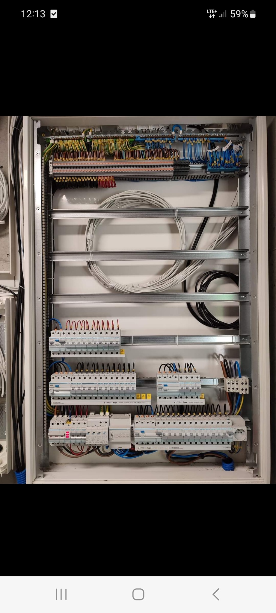 Otwarta skrzynka elektryczna z licznymi przewodami, bezpiecznikami i listwami zaciskowymi, ułożonymi równolegle na metalowych szynach wewnątrz białej obudowy.