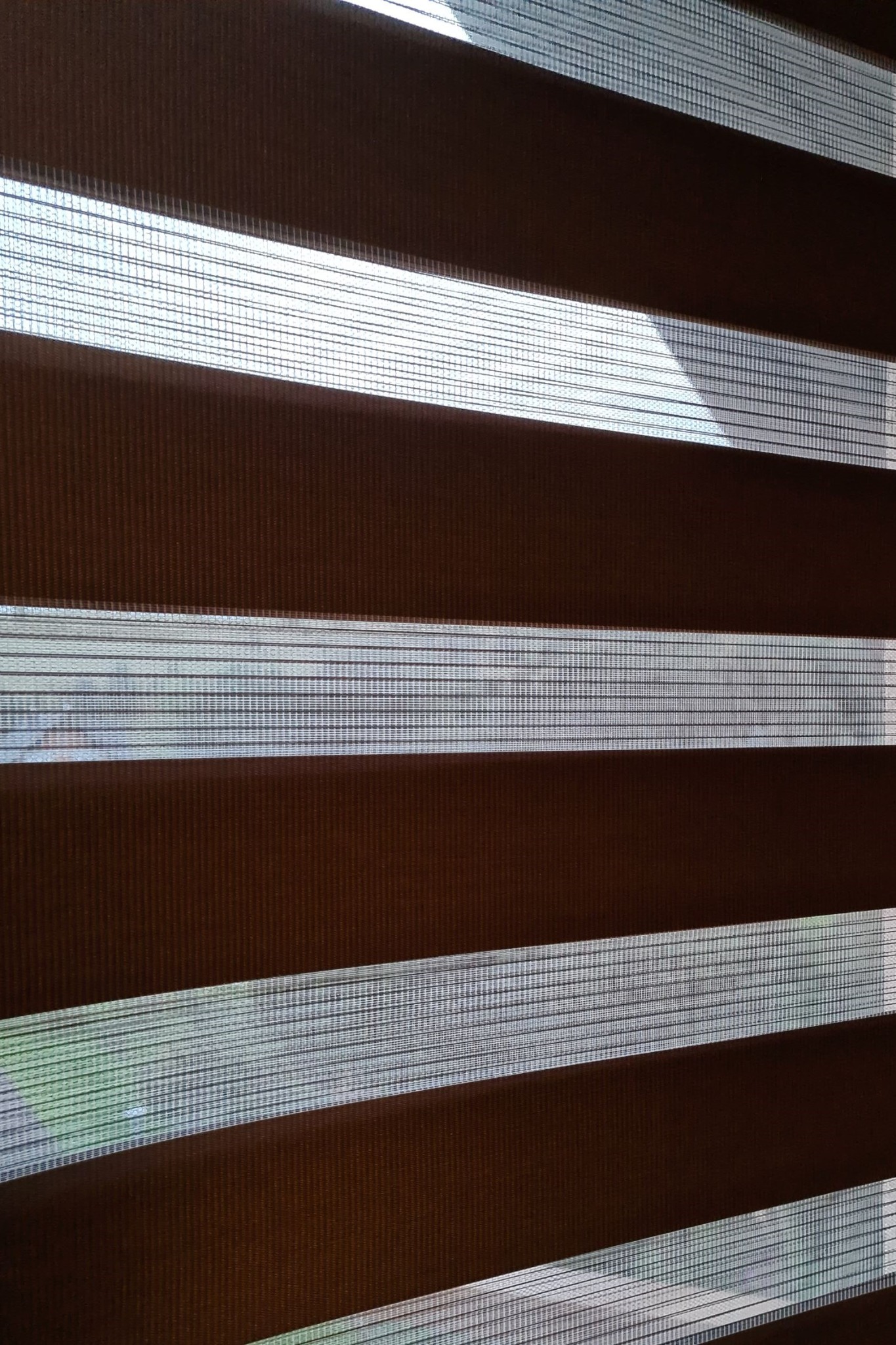 Brązowo-białe poziome pasy zaciemniające okno, widoczne delikatne prześwity światła.