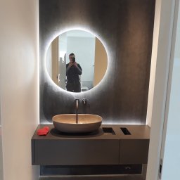 Vadym Rusetskyi - Nowoczesna łazienka z owalnym lustrem podświetlanym LED, kamienną umywalką i minimalistyczną szafką w odcieniach szarości, odbicie fotografa w lustrze.