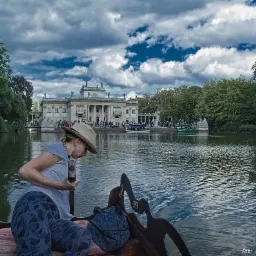 Kobieta w kapeluszu płynie ł&oacute;dką po stawie, w tle Pałac na Wodzie w Łazienkach Kr&oacute;lewskich, Warszawa.