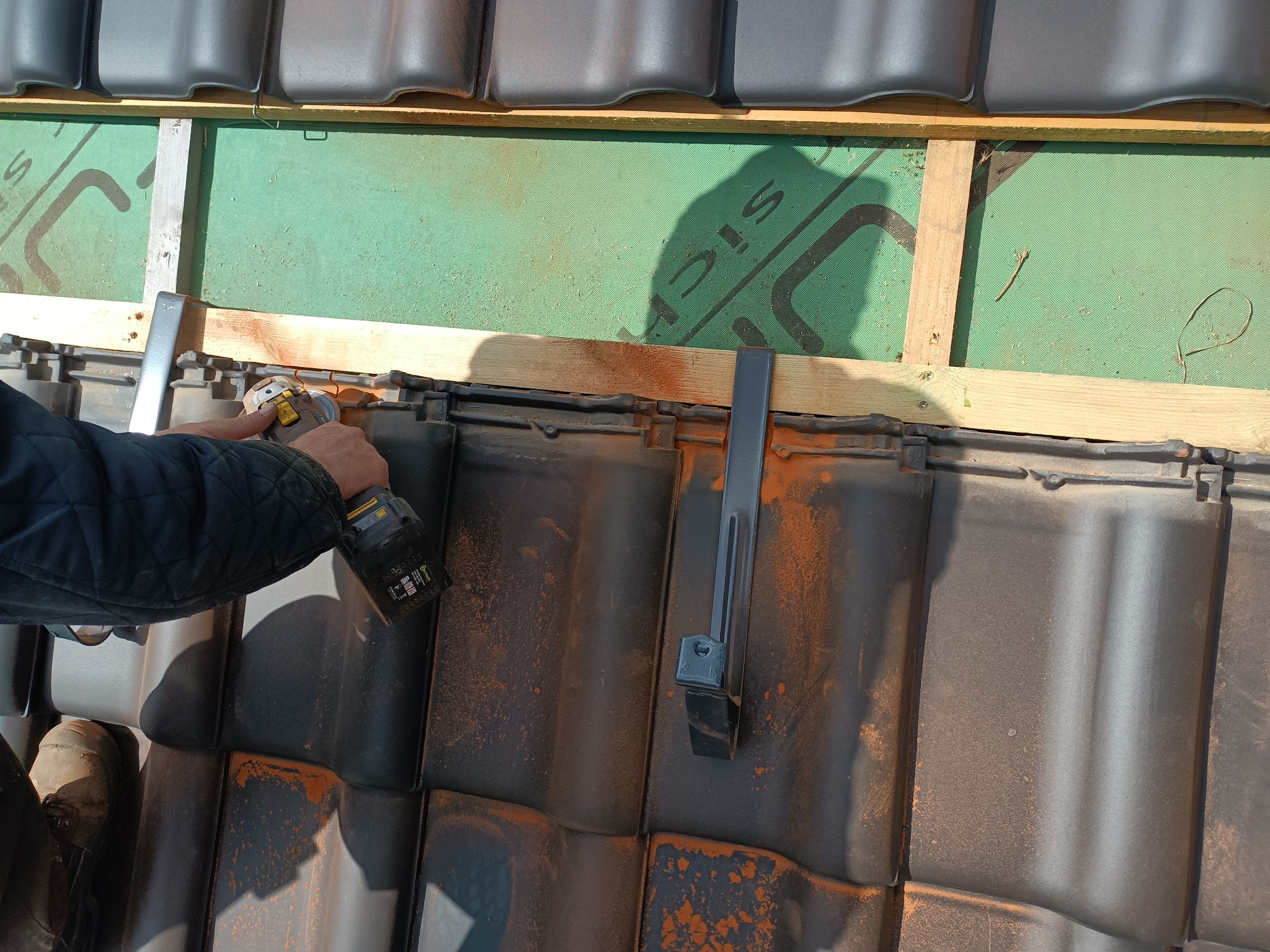 Dekarz szlifuje dachówkę szlifierką kątową podczas montażu łat i kontrłat na zielonej membranie dachowej.