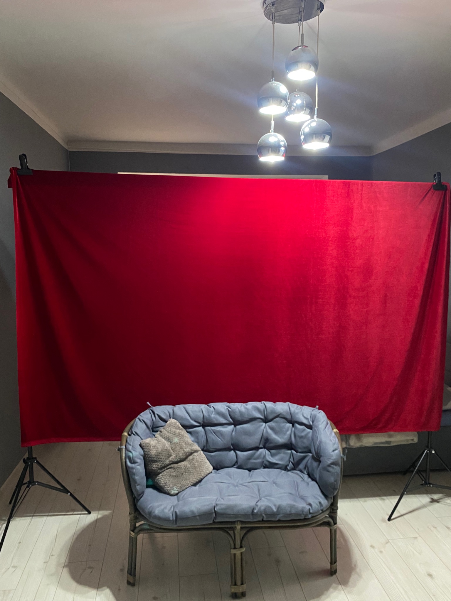 Przygotowane studio fotograficzne z czerwonym tłem, szarą sofą i lampą wiszącą