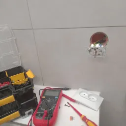 Gniazdko elektryczne wystające ze ściany łazienki, obok leży multimetr UNIT UT151C, skrzynka narzędziowa, wkrętak i złączki Wago, co wskazuje na prace elektryczne w trakcie remontu.