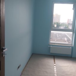 pro-finish Katarzyna Rączka - Pokój w odcieniach błękitu, świeżo po malowaniu, z zabezpieczoną podłogą folią malarską i widocznym grzejnikiem pod oknem.