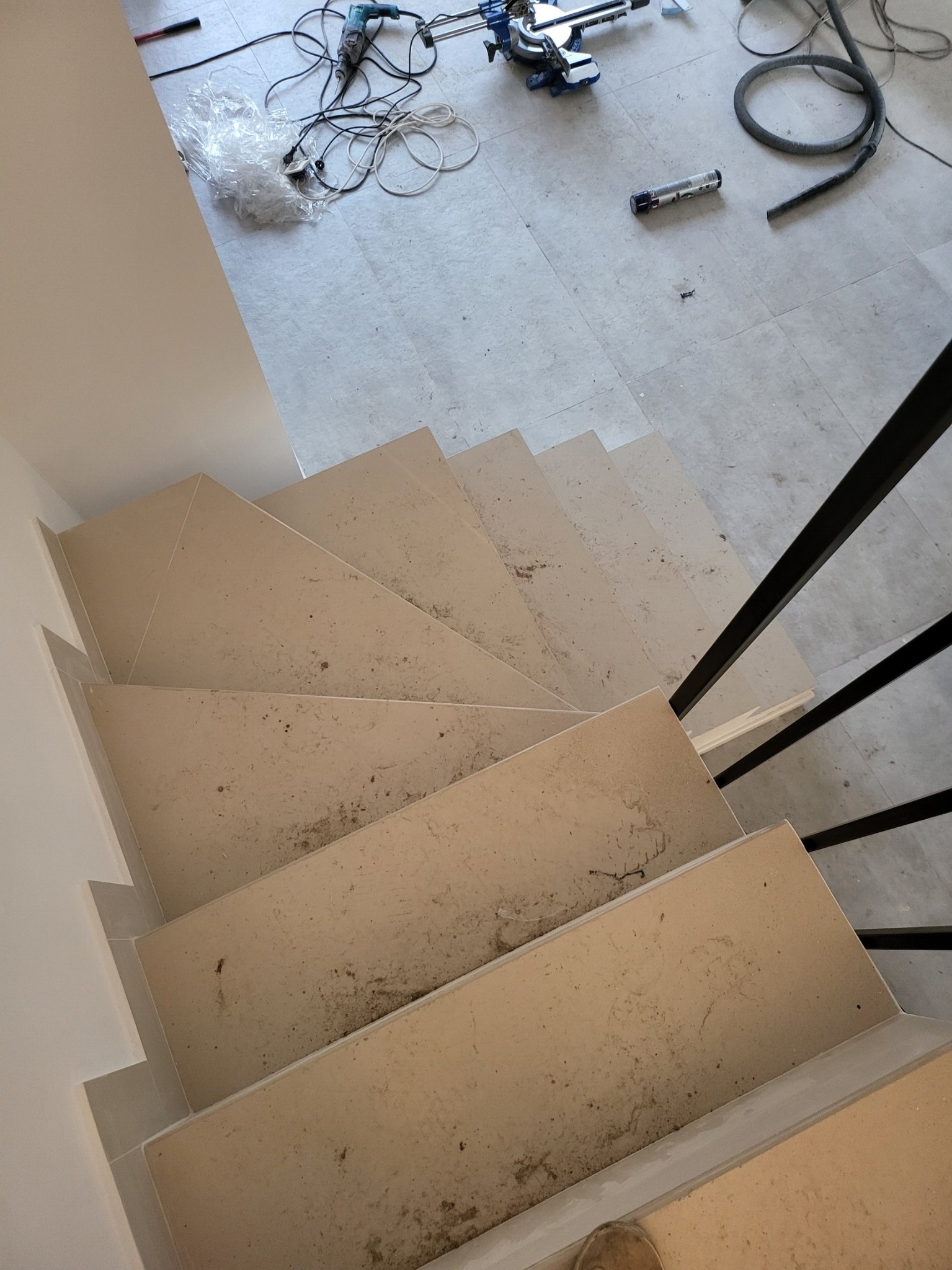 Kątowe ujęcie schodów z jasnego kamienia w trakcie montażu balustrady w Warszawie, widoczne ślady zaprawy i narzędzia na podłodze.