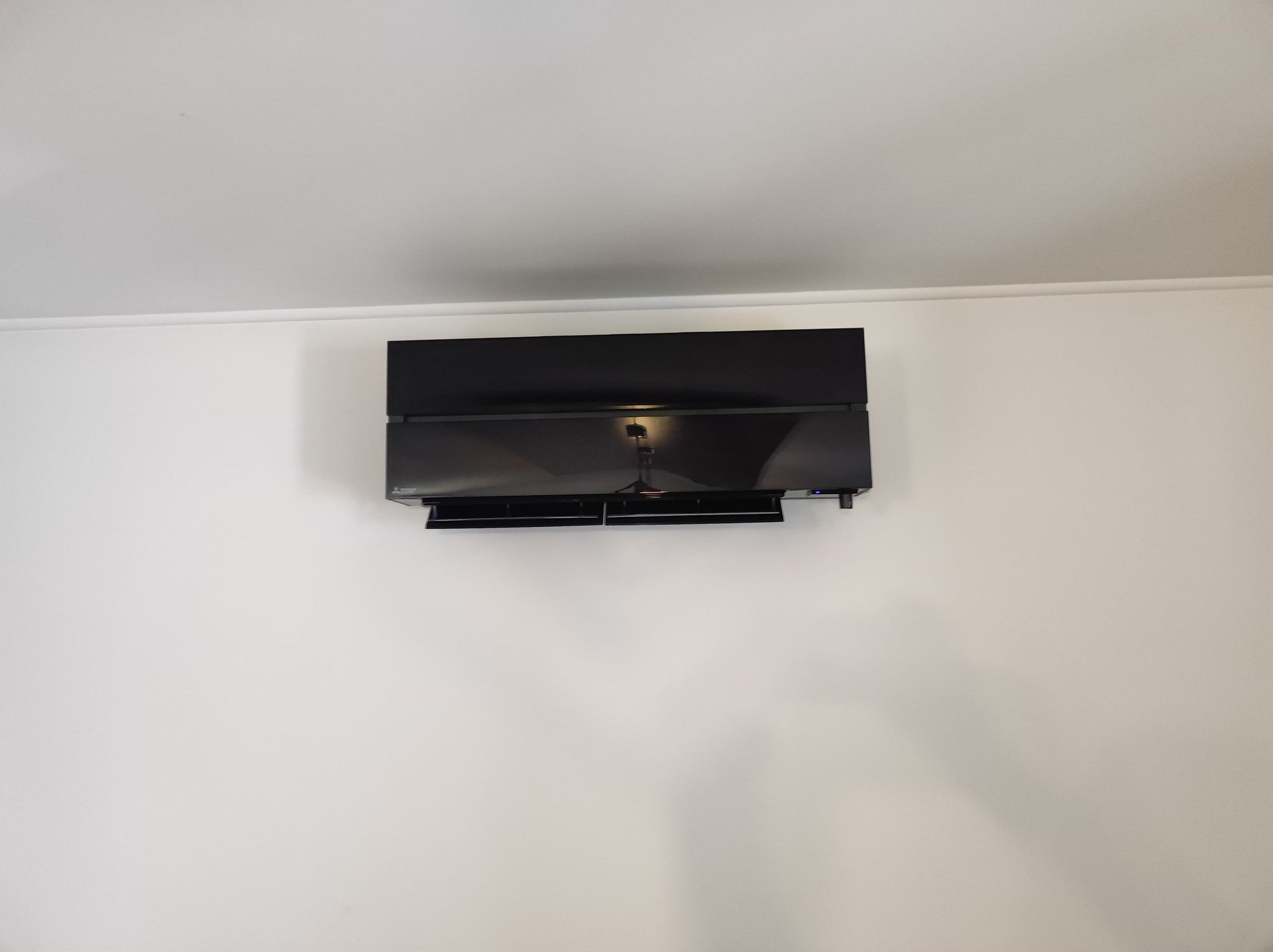 Czarna jednostka wewnętrzna klimatyzacji zamontowana na białej ścianie, widoczny fragment sufitu i listwa przypodłogowa, minimalistyczny design.