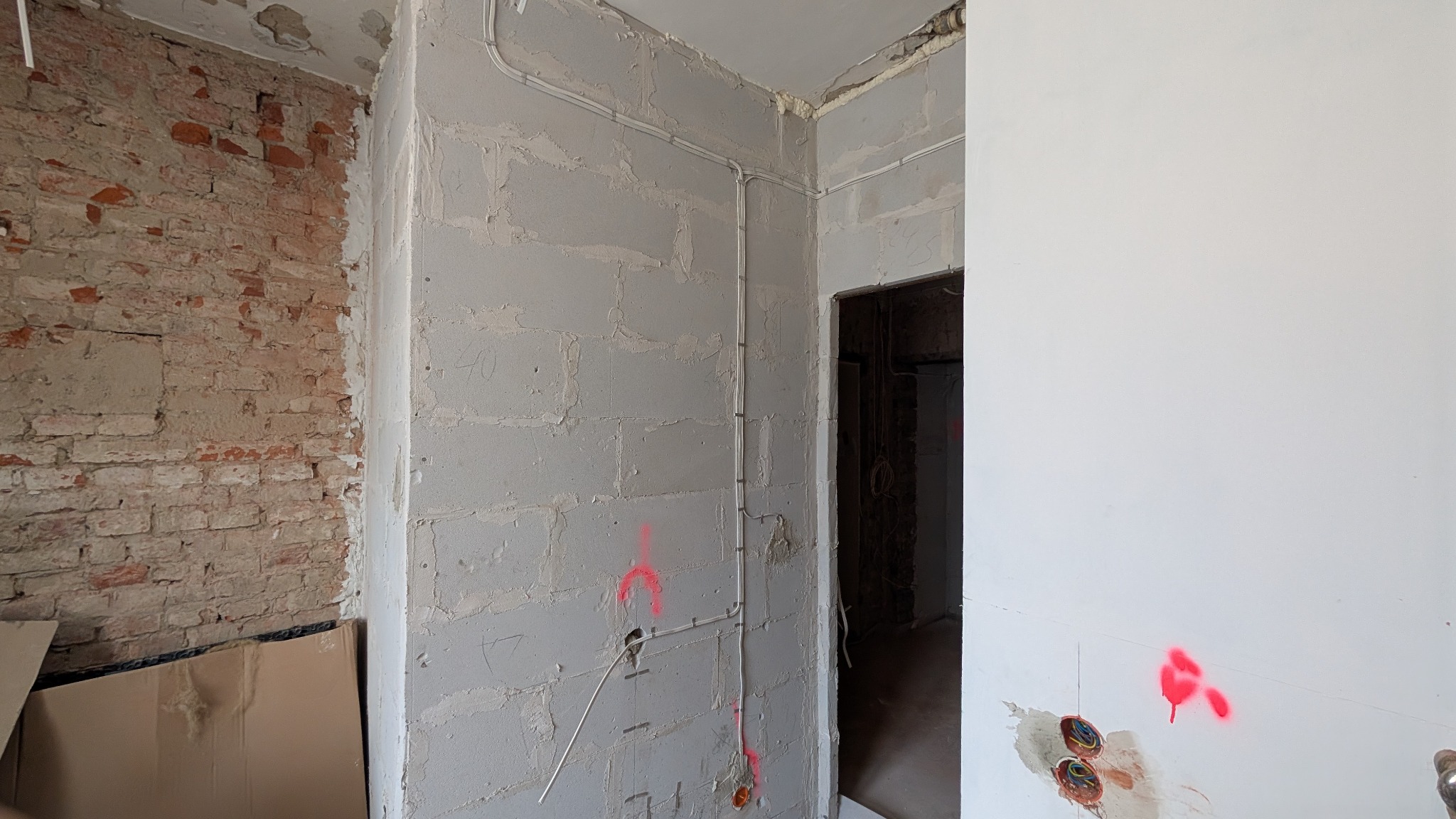 Wnętrze w trakcie remontu: surowa ceglana ściana sąsiaduje z otynkowaną ścianą z widocznymi przewodami elektrycznymi, znakami poziomów i przygotowanymi otworami pod gniazdka.