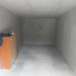 Surowe wnętrze pomieszczenia z szarymi ścianami i podłogą, widoczne ślady po gładzi na ścianach i suficie, szafka z boku.