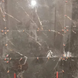 Montaż ciemnych, marmurkowych płytek ściennych z użyciem poziomicy, krzyżyków dystansowych i sznurka pionowego; widoczne narzędzia glazurnicze na podłodze.