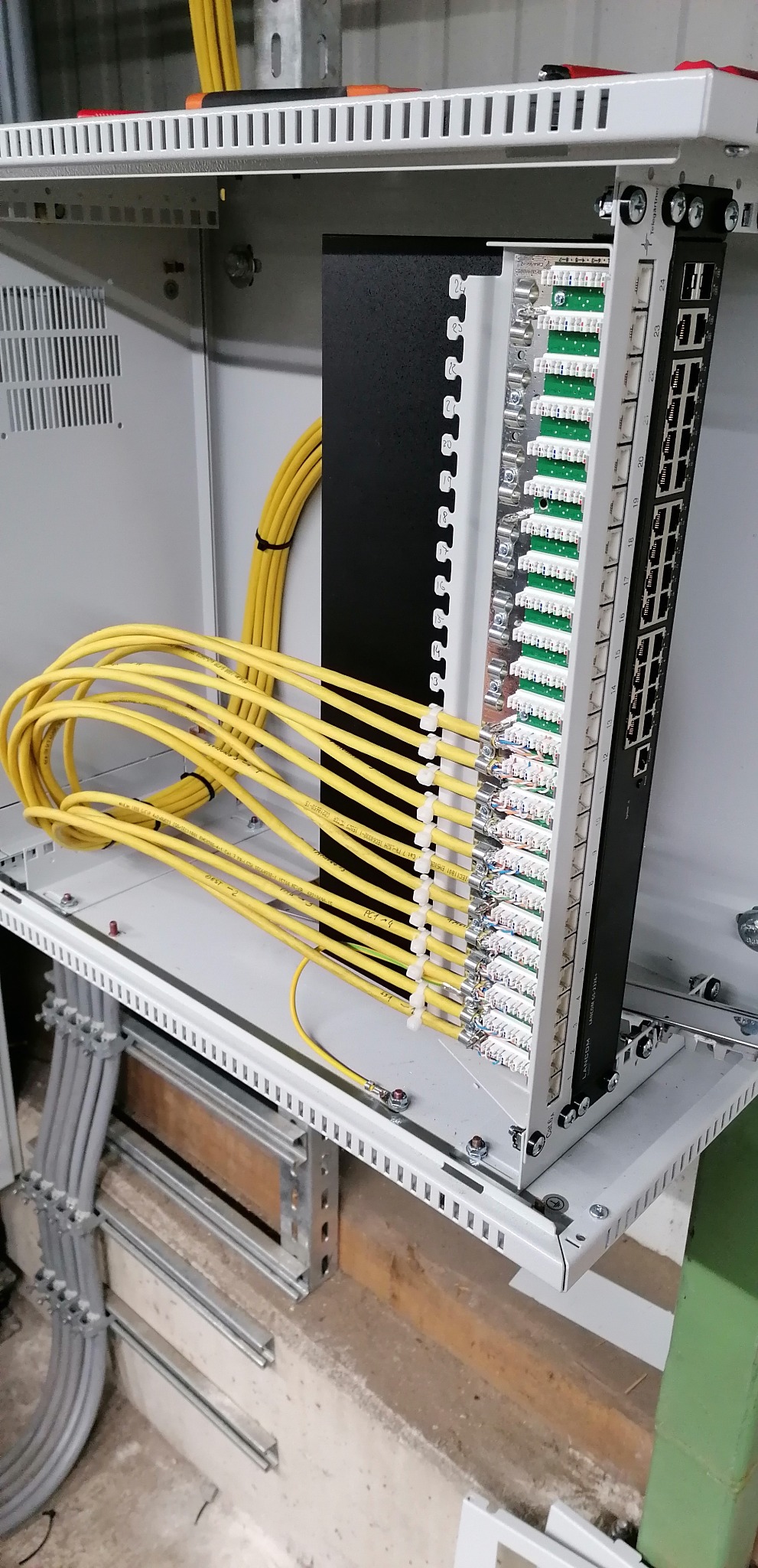 Panel krosowniczy z podłączonymi żółtymi kablami sieciowymi wewnątrz szafy rack, widoczne oznaczenia portów.