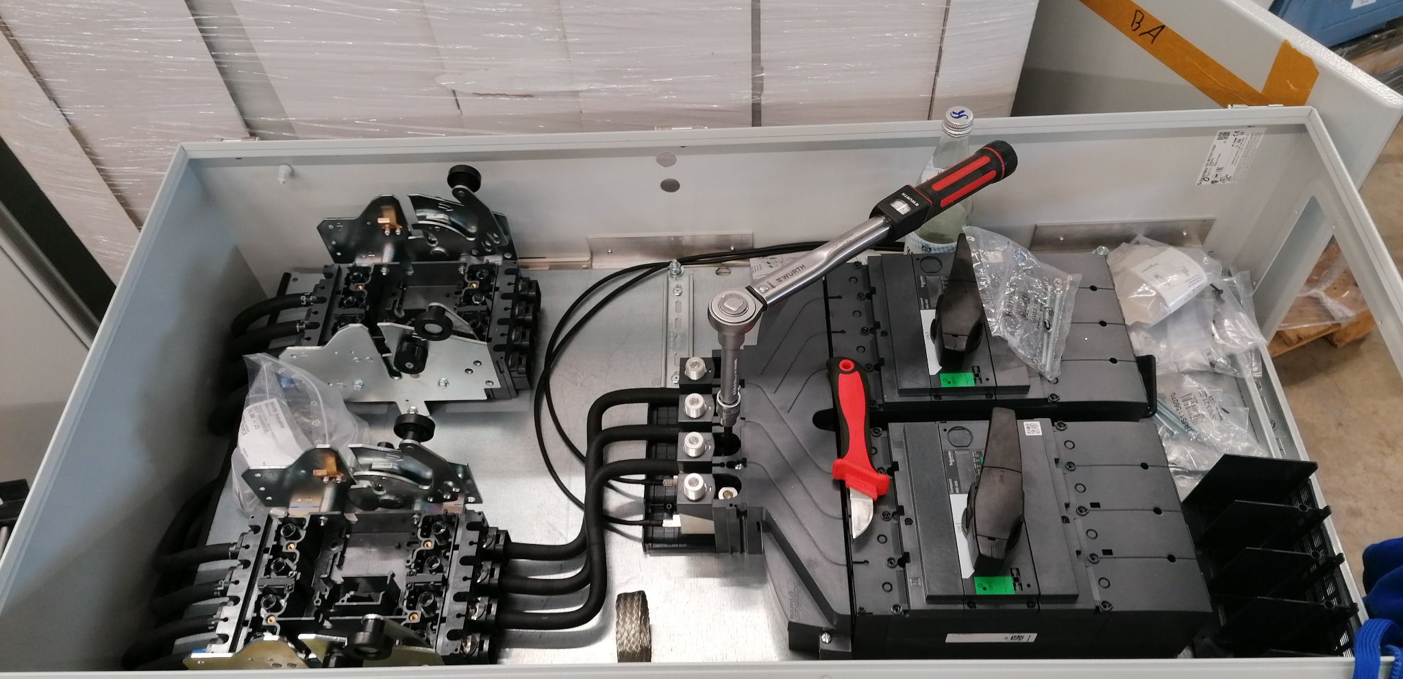 Wnętrze szafy elektrycznej w trakcie montażu, widoczne elementy instalacji, klucz dynamometryczny marki Würth, nożyk z czerwoną rękojeścią i butelka wody mineralnej.
