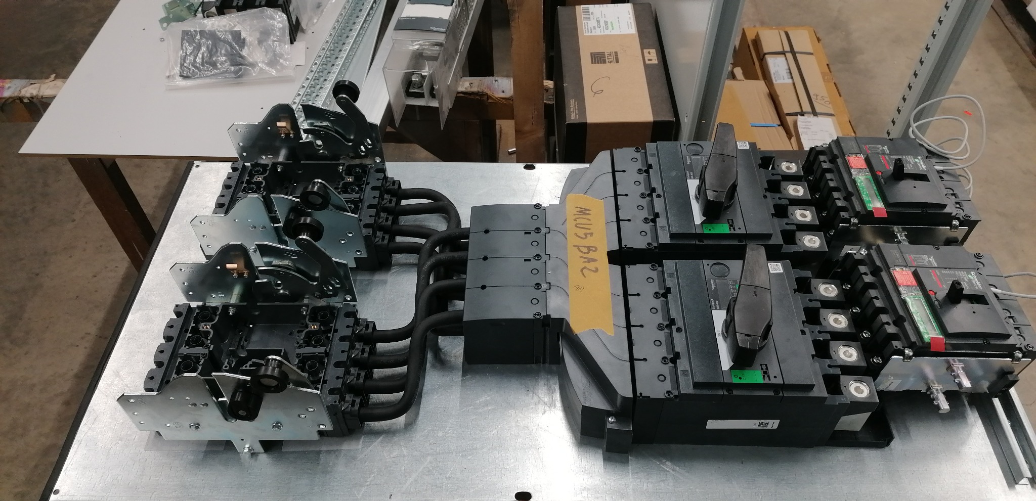 Rozdzielnica elektryczna z wyłącznikami, widoczne okablowanie i elementy montażowe na metalowym stole warsztatowym.