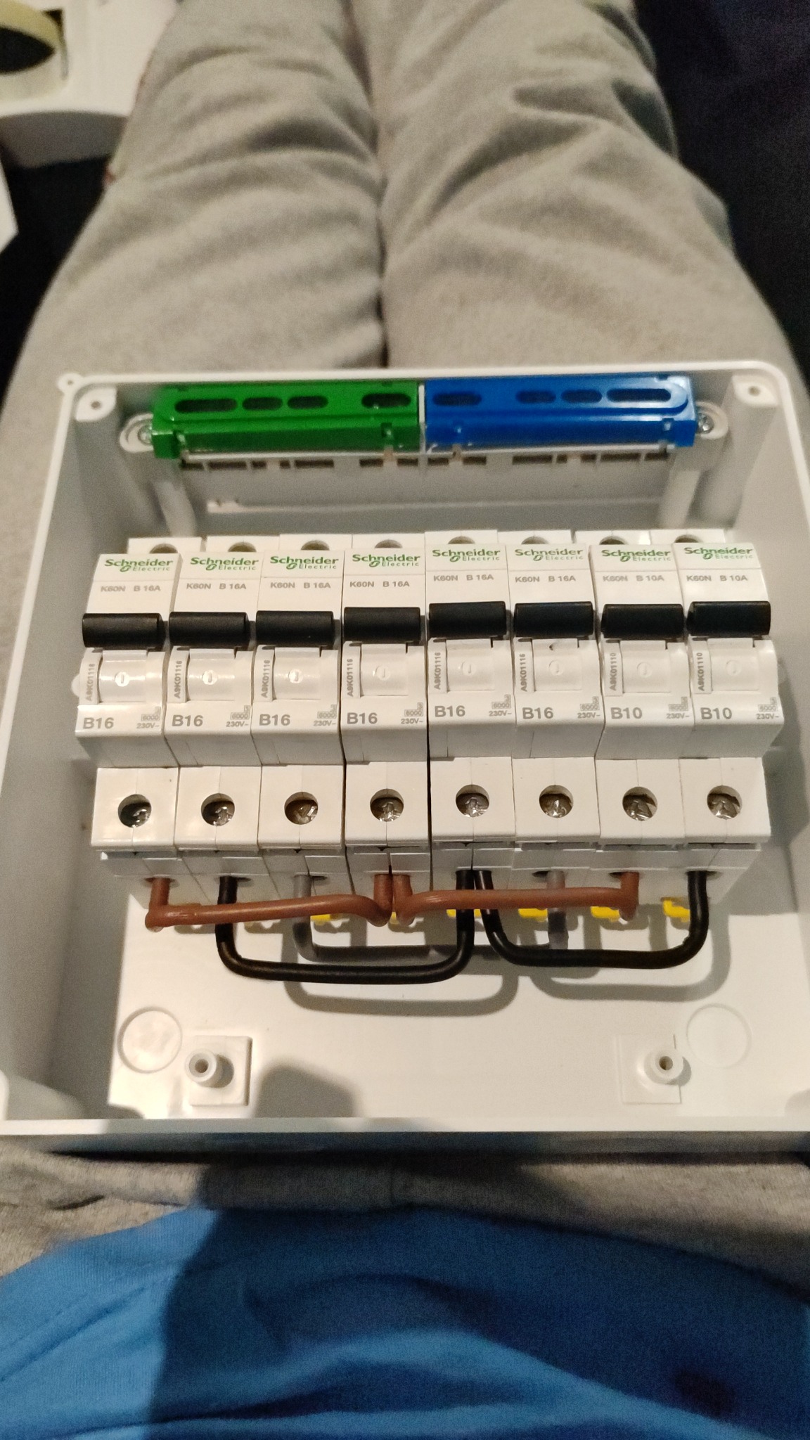 Rozdzielnica elektryczna z zainstalowanymi bezpiecznikami Schneider Electric, widoczne przewody w kolorach czarnym, brązowym i żółtym, zamontowane na szynie DIN w białej obudowie, z widocznymi...