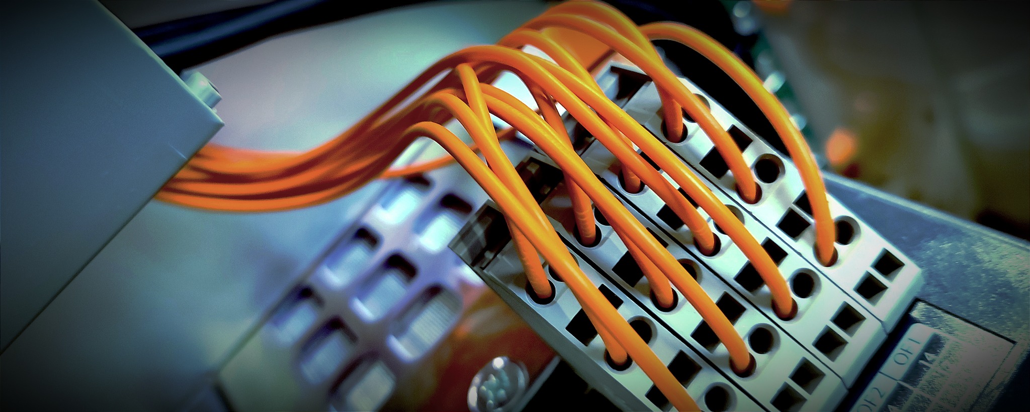 Pomarańczowe przewody wpięte w listwę zaciskową, widoczne oznaczenia na obudowie urządzenia.