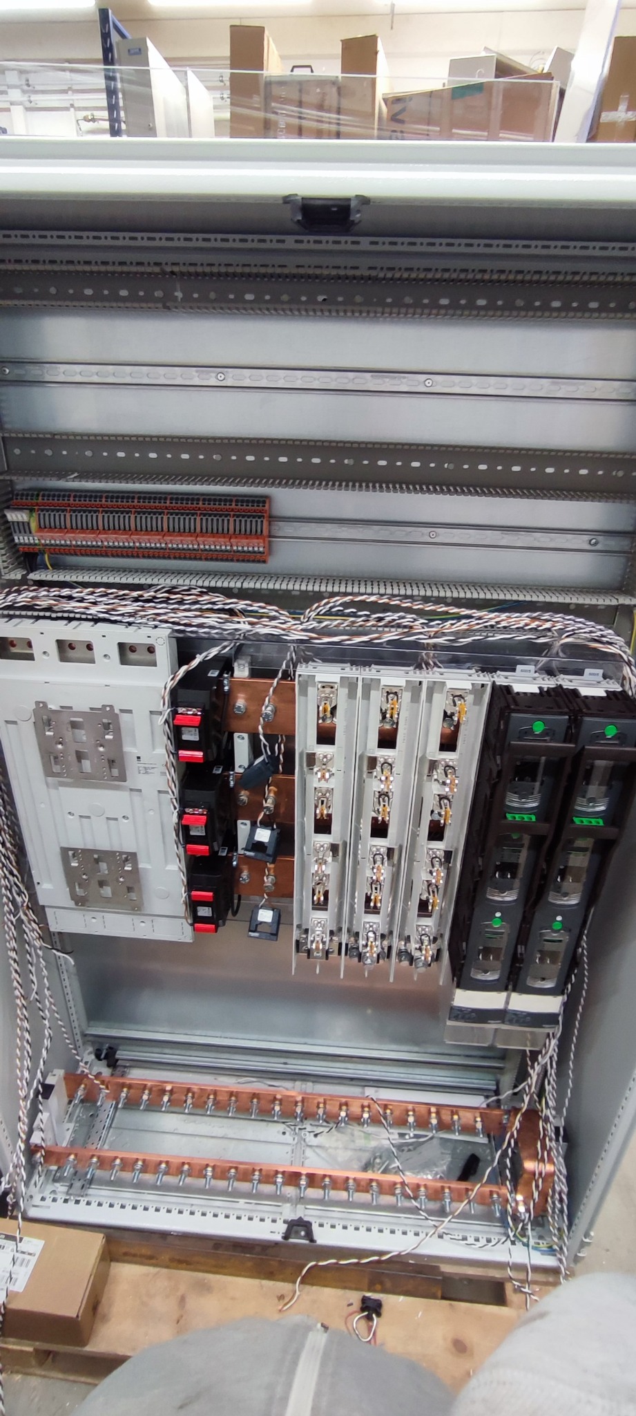 Otwarta metalowa szafa elektryczna w trakcie montażu, widoczne liczne kable, bezpieczniki, listwy zaciskowe i miedziane szyny, częściowo podłączone przewody w biało-czarnym oplocie.