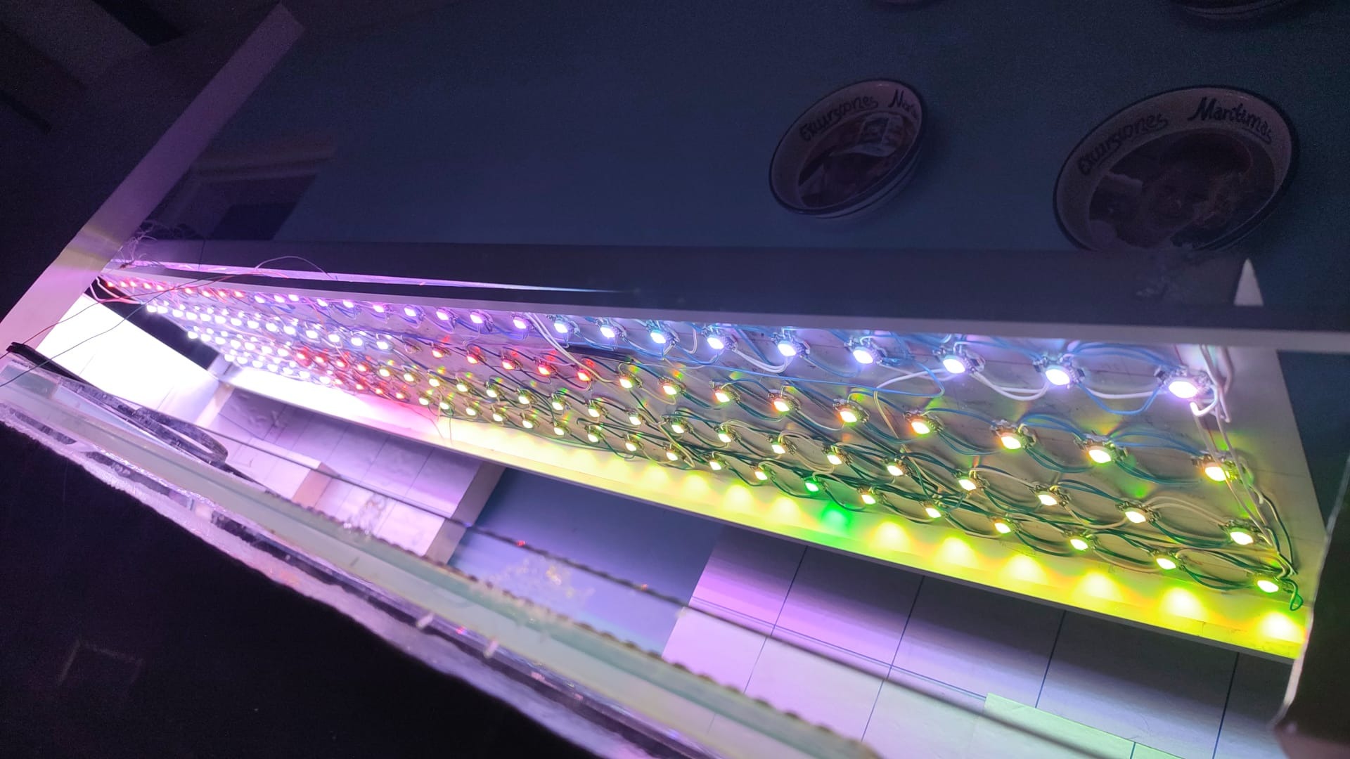 Rzędy kolorowych diod LED zamontowane pod sufitem, widoczne przewody i elementy konstrukcyjne, w tle dekoracyjne talerze na suficie.