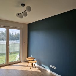 DP REM-BUD DANIEL PŁACHECKI - Pokój po remoncie: ciemnoniebieska ściana, drewniana podłoga, białe listwy przypodłogowe, nowoczesna lampa sufitowa z kulistymi kloszami, okno balkonowe z widokiem na ogród, dwa małe drewniane...