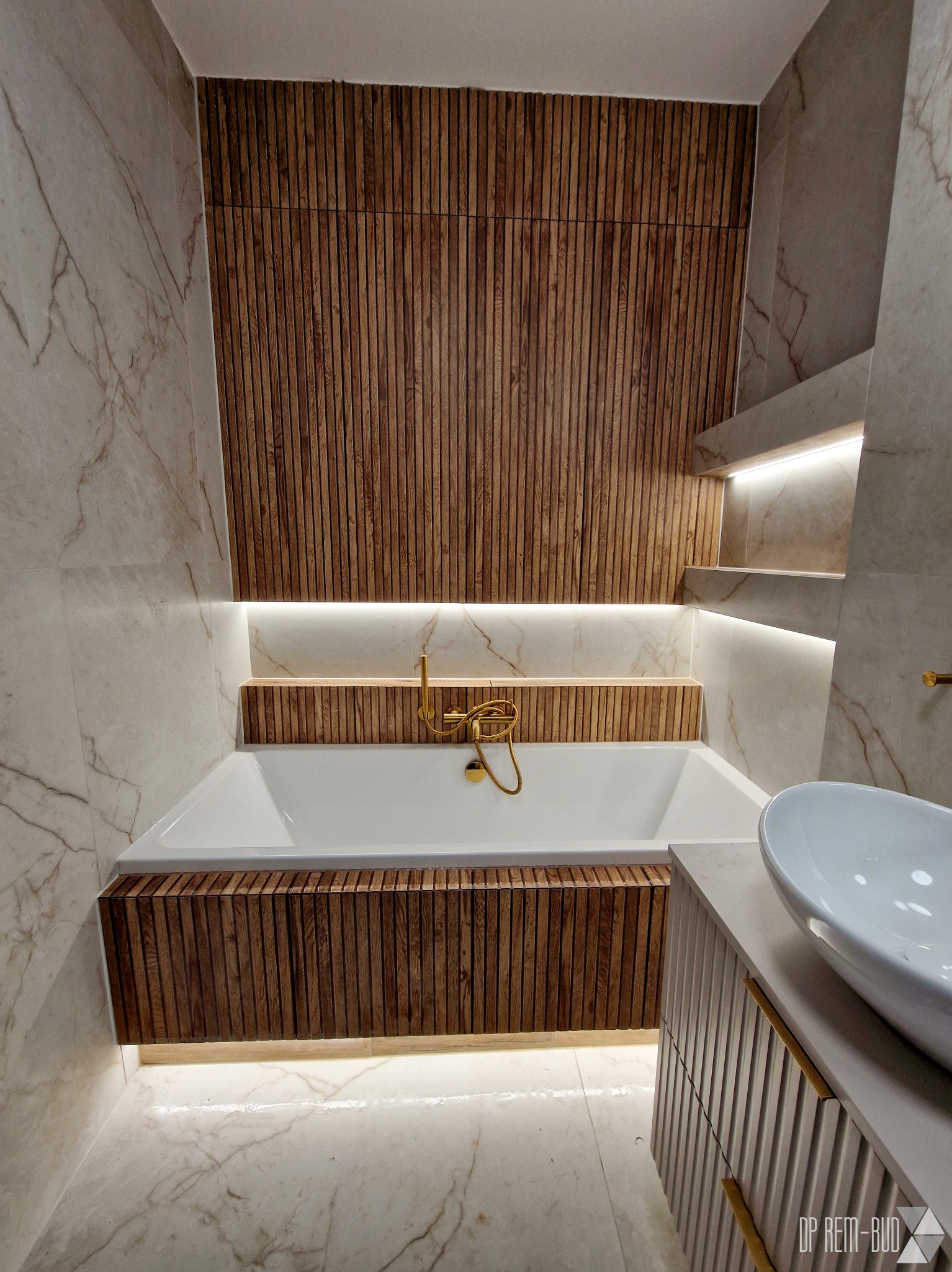 Nowoczesna łazienka z marmurowymi płytkami, drewnianymi lamelami, podświetlaną wanną i złotą armaturą.