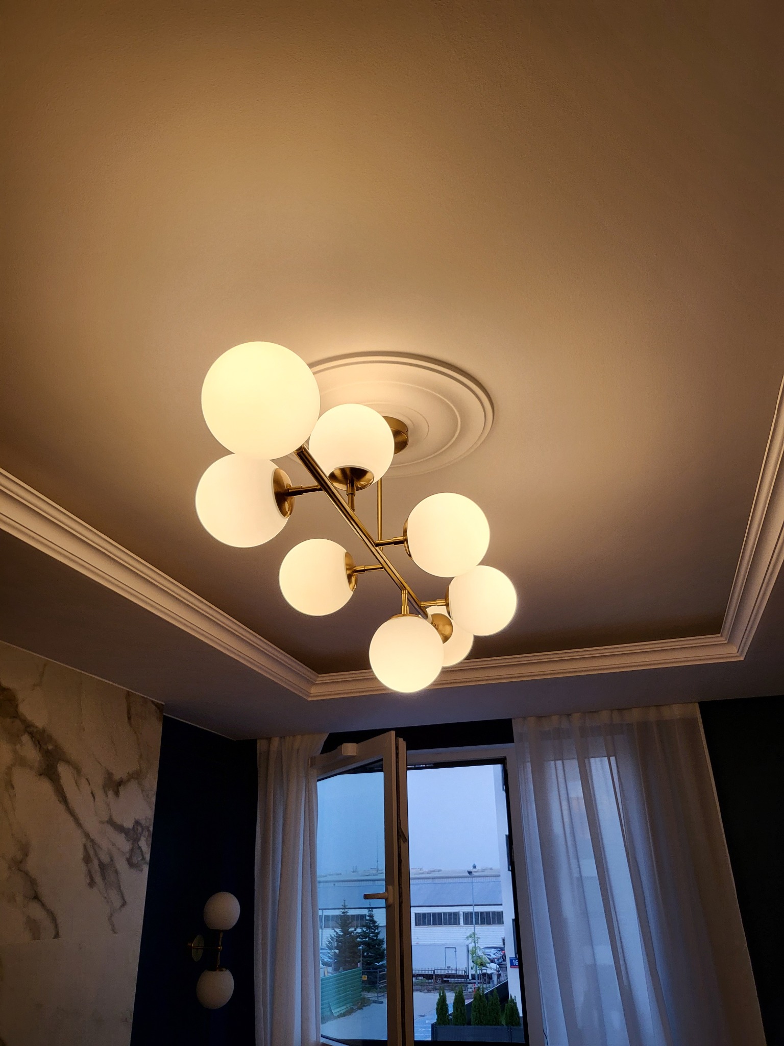 Nowoczesny żyrandol z kulistymi, mlecznymi kloszami, zamontowany na suficie z dekoracyjną sztukaterią i listwami przysufitowymi w wyremontowanym wnętrzu.