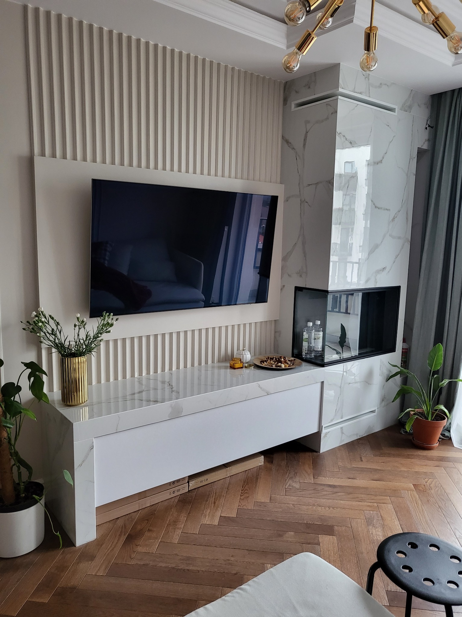 Nowoczesny salon z telewizorem na ścianie z dekoracyjnymi panelami, marmurowym kominkiem i parkietem w jodełkę.