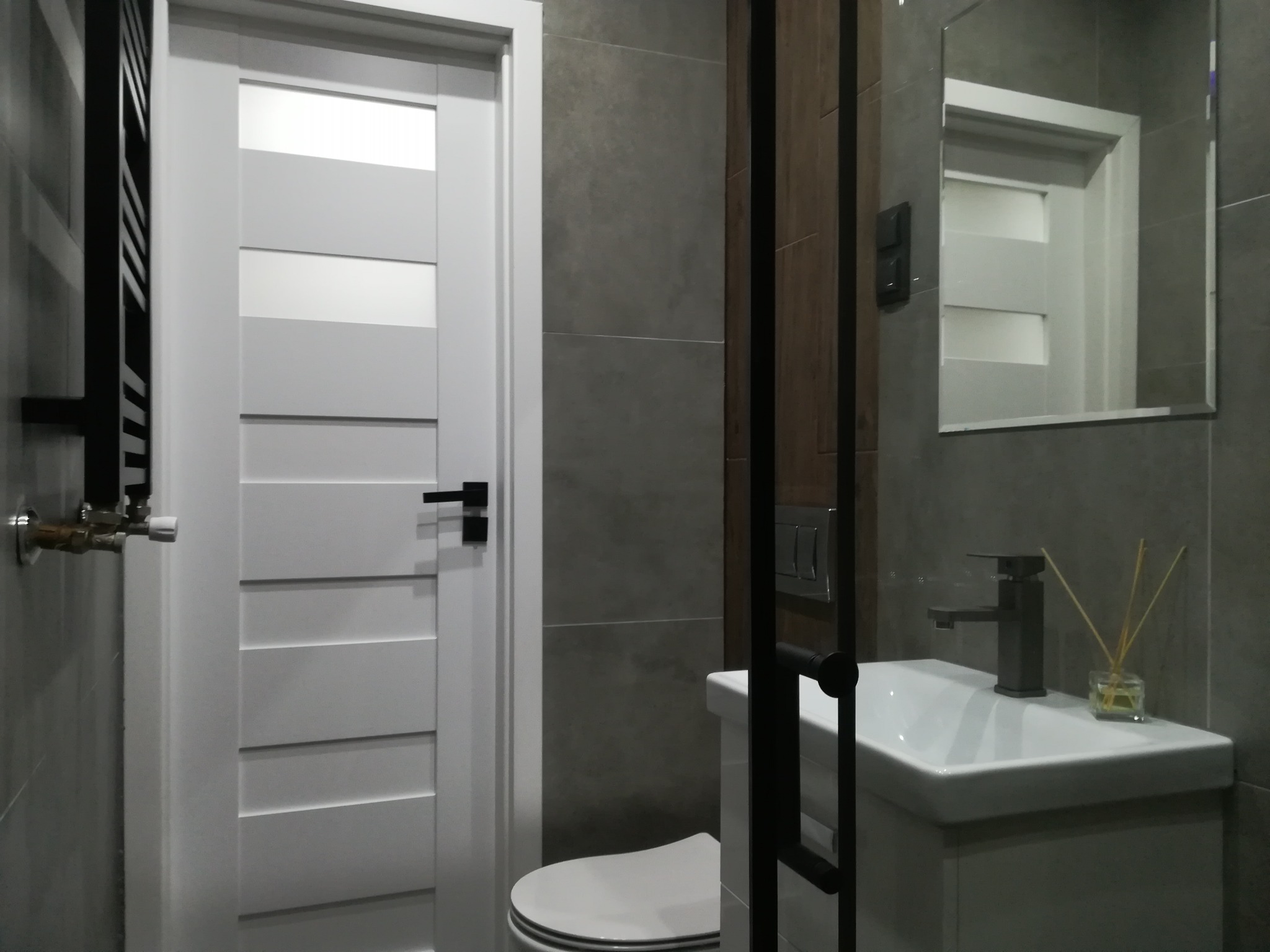 Nowoczesna łazienka w szarościach z białymi drzwiami z poziomymi panelami, umywalką nablatową i minimalistyczną armaturą.