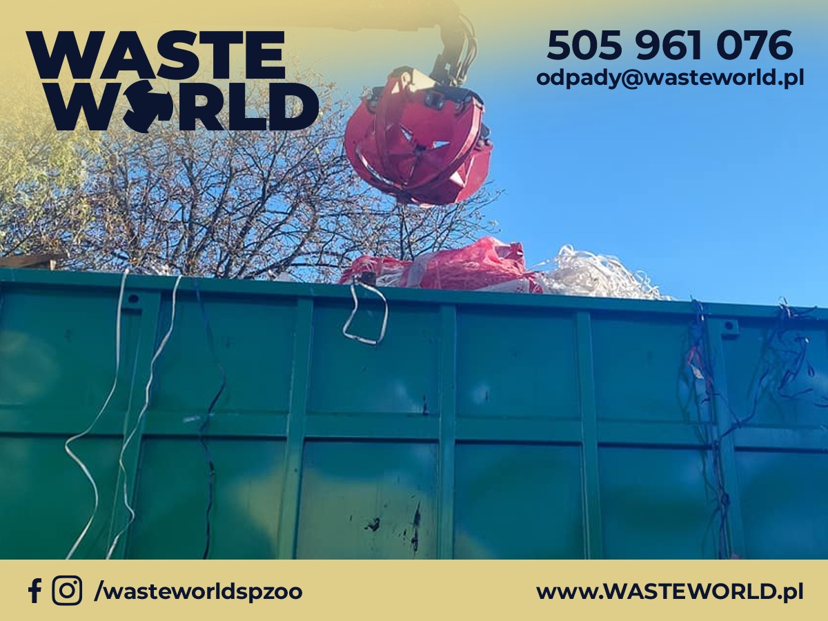 Czerwony chwytak mechaniczny umieszcza odpady w zielonym kontenerze. Widoczne opakowania z tworzyw sztucznych i inne odpady. W tle błękitne niebo i drzewa.