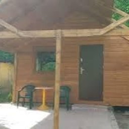 Gretter sp z oo firma elektryczno budowlana - Niewielka, drewniana konstrukcja z płaskim dachem w trakcie budowy, widoczne elementy szkieletu dachu, z boku mały kamienny grill, obok stolik i krzesła.