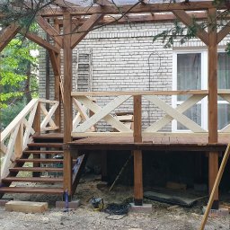 Gretter sp z oo firma elektryczno budowlana - Drewniany taras z pergolą w trakcie budowy, widoczne schody, balustrady z krzyżowym wzorem, narzędzia i materiały budowlane wokół.