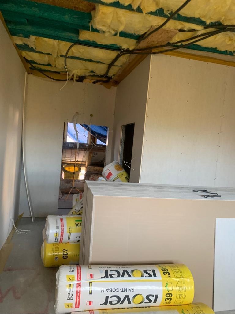 Wnętrze w trakcie wykańczania: izolacja stropu wełną mineralną, ściany obłożone płytami kartonowo-gipsowymi, materiały budowlane Isover na podłodze.