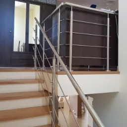 Nierdzewna balustrada schodowa z poziomymi poprzeczkami, widok z dołu schodów, w tle szafa z lustrem.