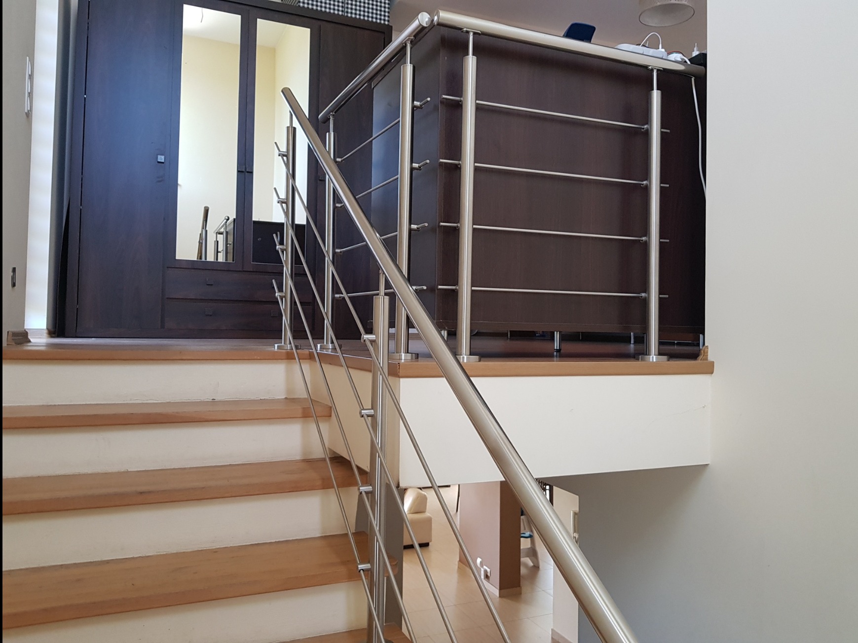Nierdzewna balustrada schodowa z poziomymi poprzeczkami, widok z dołu schodów, w tle szafa z lustrem.