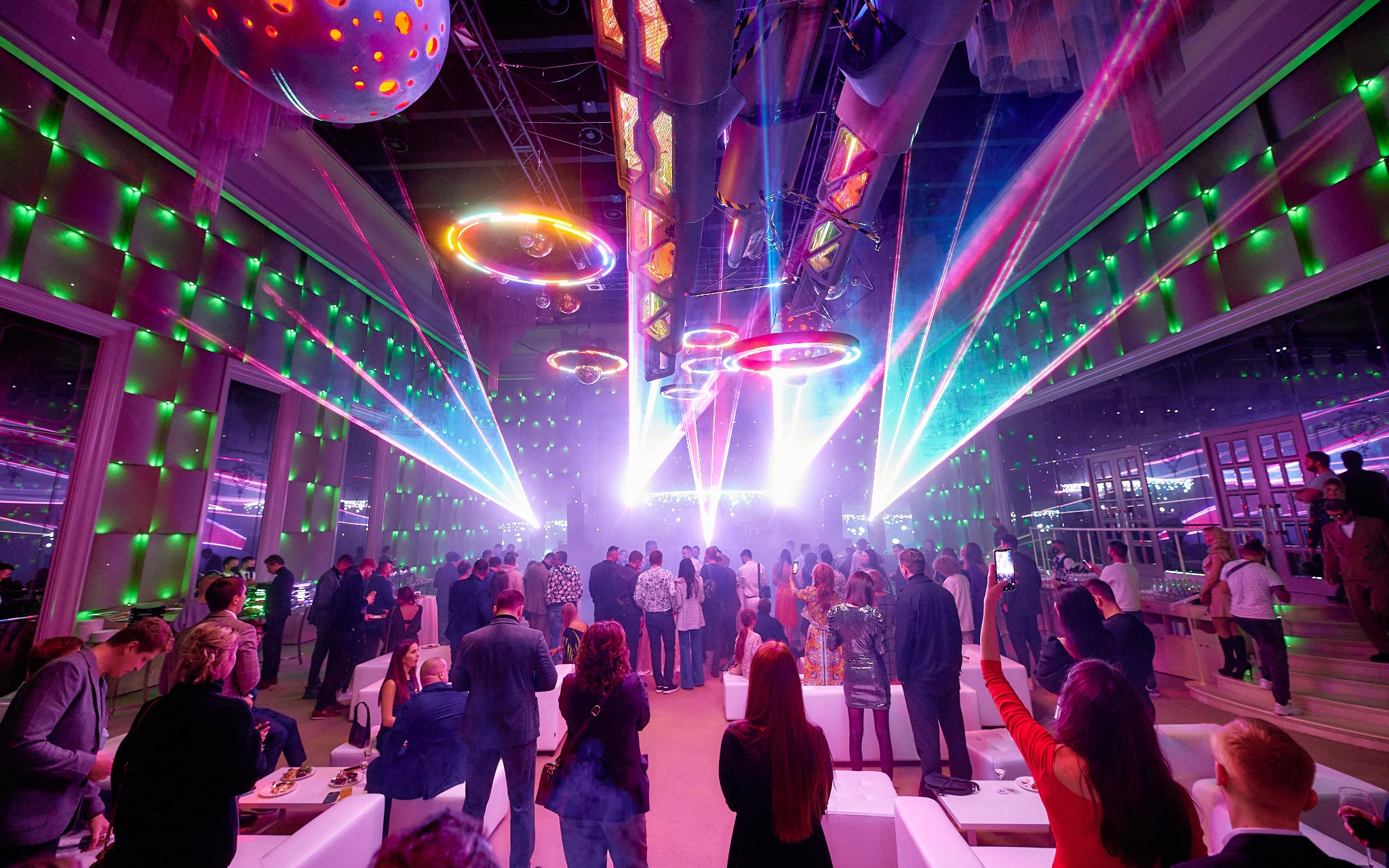 Wnętrze sali balowej podczas imprezy z efektami świetlnymi, widoczni goście i dekoracje.
