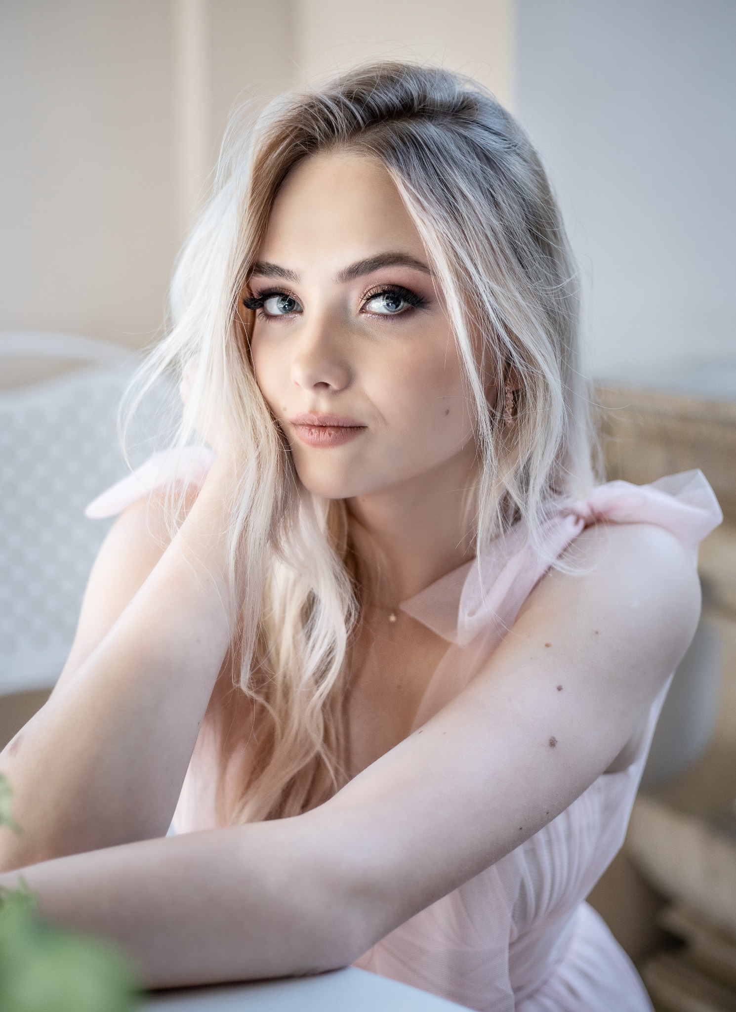 Portret kobiety z platynowymi blond włosami w zwiewnej, różowej sukience. Delikatny makijaż podkreśla jej niebieskie oczy.