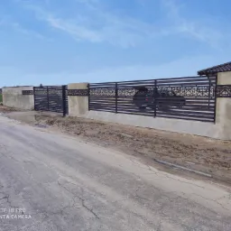 Nowoczesne ogrodzenie panelowe z elementami dekoracyjnymi i betonowymi słupkami, widok z ulicy, błoto po deszczu.