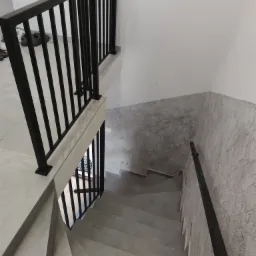 Wewnętrzne schody z szarymi stopniami i czarną, metalową balustradą, widok z góry, ściany wykończone dekoracyjnym tynkiem imitującym beton.